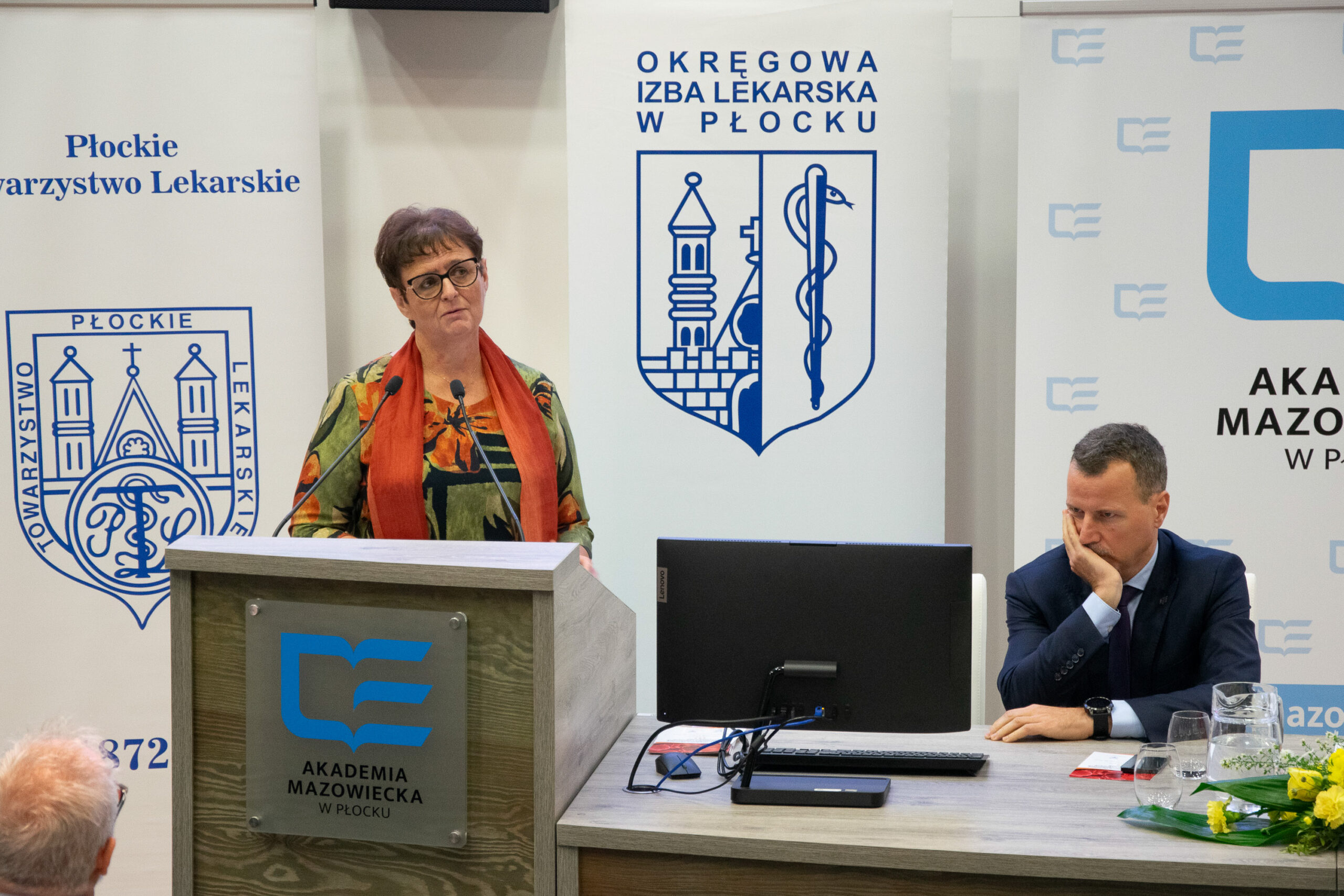 kobieta mówiąca do mikrofonu , stojąca przy mównicy 