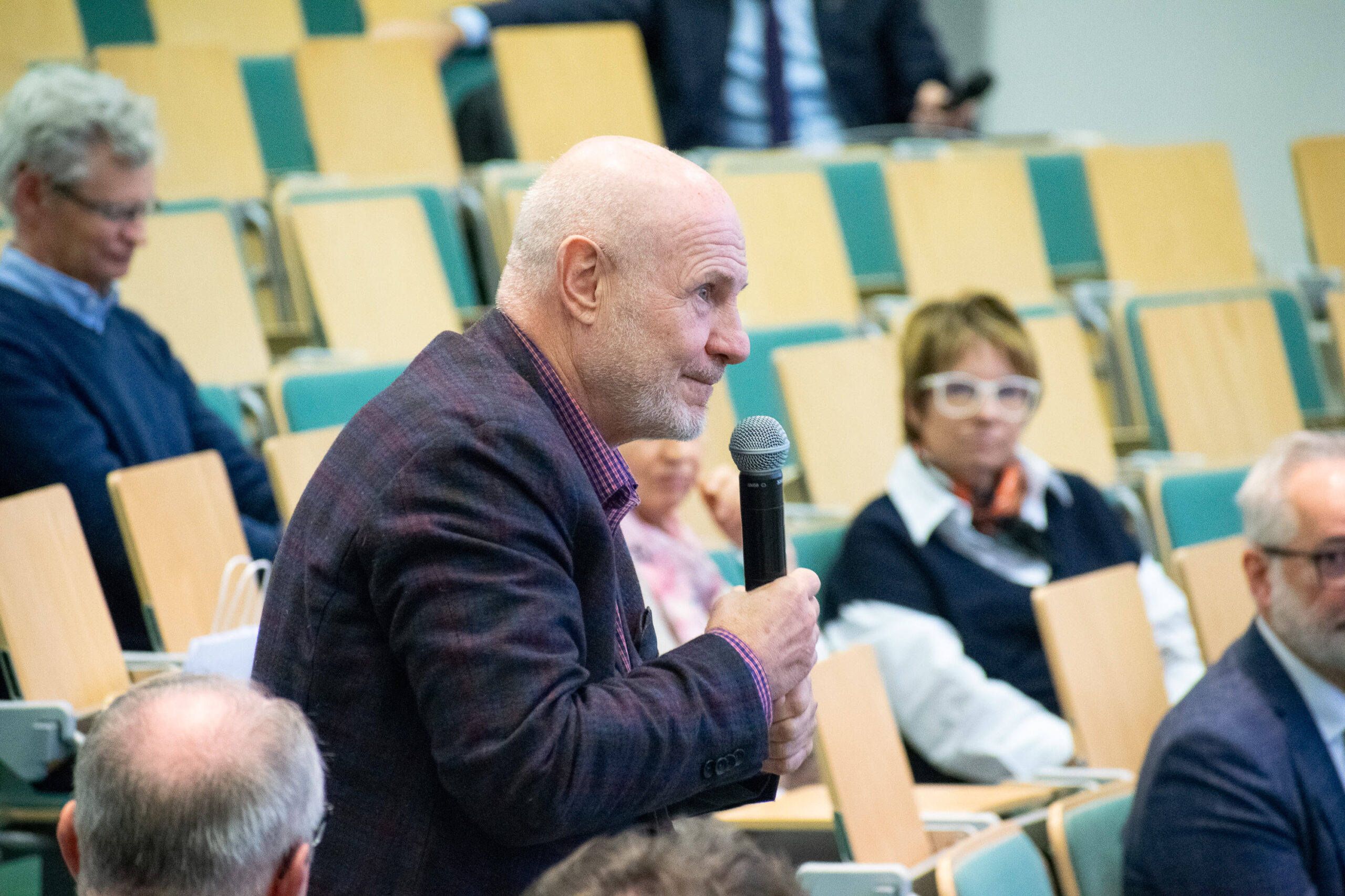 mężczyzna stojący bokiem, mówiący do mikrofonu