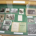 Gablota z artefaktami, stare zdjęcia, księga i zapisy.