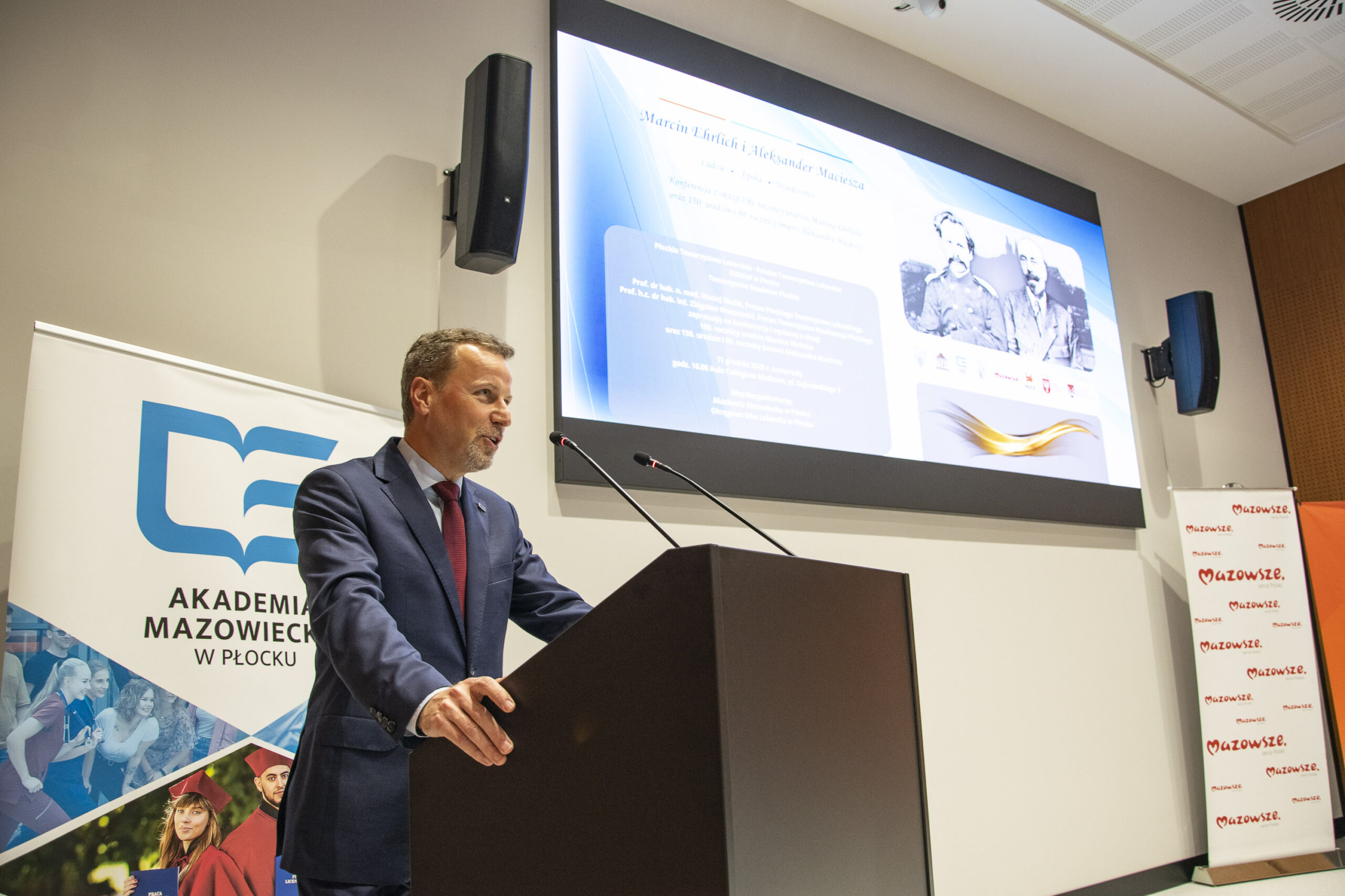 Rektor stojący przy mównicy, za nim rollap